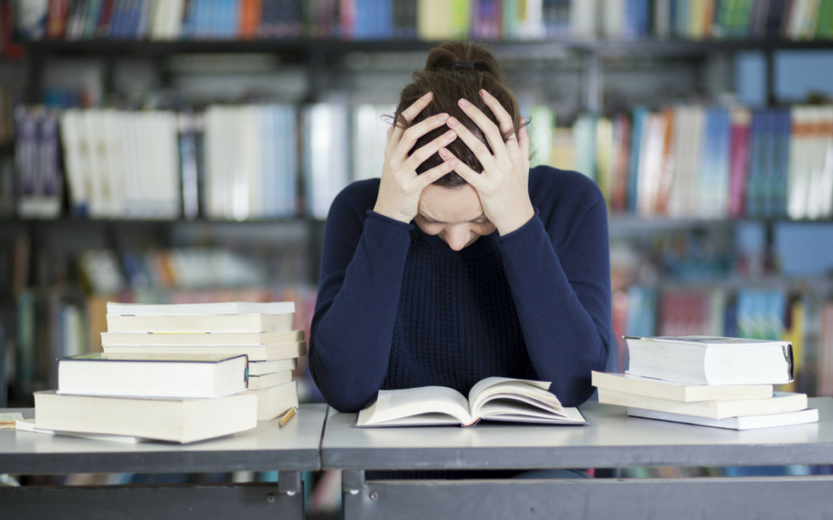 girl sat over books with head in hands experiencing period pain at school