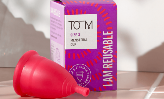 TOTM's size 3 menstrual cup unboxed and lying beside the packaging box on top of pink tiles