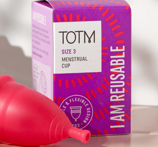 TOTM's size 3 menstrual cup unboxed and lying beside the packaging box on top of pink tiles